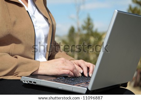 Wireless computer use outdoors by a businesswoman on a sunny day (shallow focus point on foreground hand).