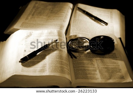 Christian bible study image in sepia tint and high contrast - two bibles with pens and a magnifying glass (shallow focus point on foreground pen, bible, and magnifying glass).
