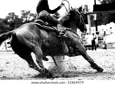 High contrast, black and white closeup of a rodeo Barrel Racer making a turn at one of the barrels (shallow focus on horse and exploding sand).