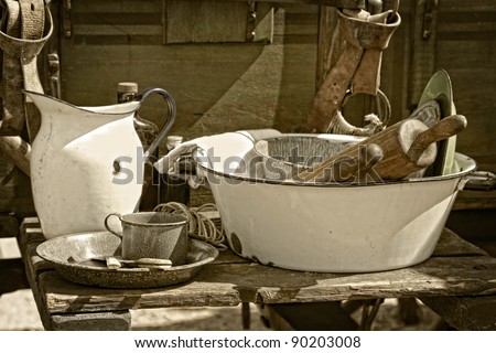 Still life image of vintage cooking utensils and dishes beside an authentic American old west style chuck wagon at an outdoor cooking demonstration (sepia tint added).