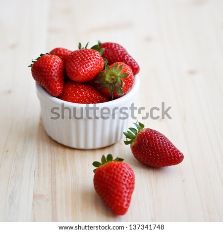 Strawberries in a white cocotte on a wooden table, square