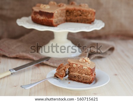 Homemade coffee and walnut cake on a stand with a cut out piece, selective focus