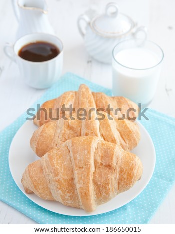 Two croissants with coffee and milk on the white wooden table