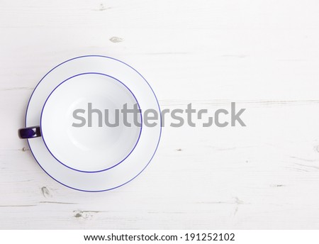 Empty cup and saucer on a white wooden table, view from top