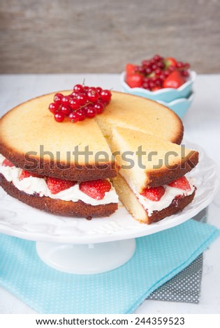 Victoria sponge cake with buttercream frosting, jam and strawberries on the stand with cut slice, selective focus