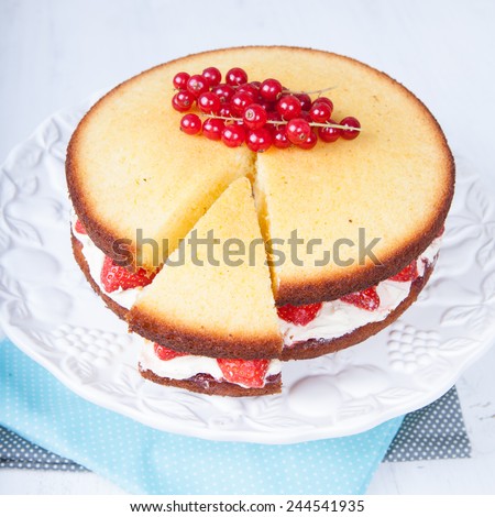 Victoria sponge cake with buttercream frosting, jam and strawberries with cut slice on the stand, selective focus