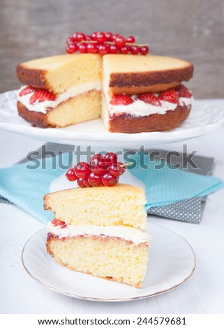 Victoria sponge cake with buttercream frosting, jam and strawberries on the stand with cut slice, selective focus