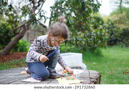 A little girl in the garden sitting on the log drawing, selective focus