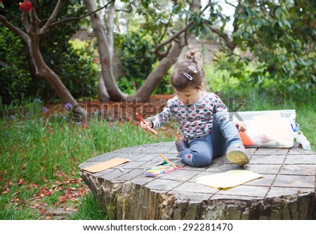 A little girl in the garden sitting on the log drawing