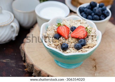 Breakfast in the garden: oatmeal cereals with berries on the dark wooden table, selective focus