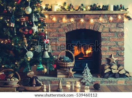 Christmas tree, various decorations in the basket in front of the fireplace with burning fire, candles and baubles, selective focus; dark vintage style toned photo