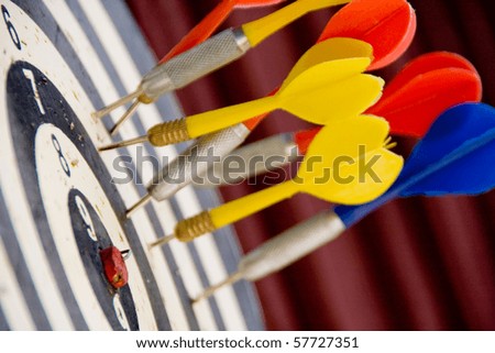 Close shot of red, yellow and blue darts stuck in a dart board but not in the bulls eye