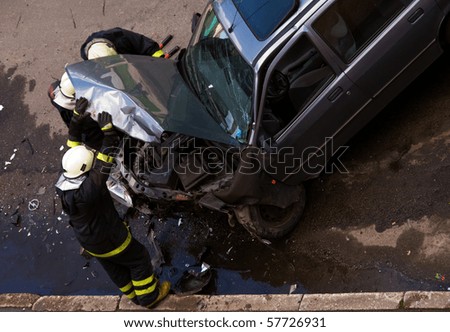 Firemen at traffic accident site, checking car, holding engine hood open