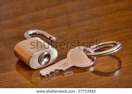 Small metal padlock with key on wooden surface