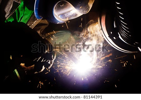 Welder with welding helmet working hard, sparks and smoke around him
