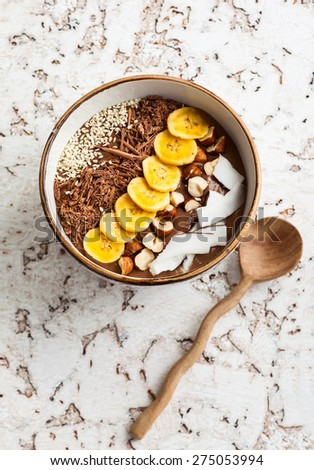 Chocolate hazelnut smoothie bowl topped with sliced banana, shredded coconut, chopped  chocolate, nuts and sesame seeds.