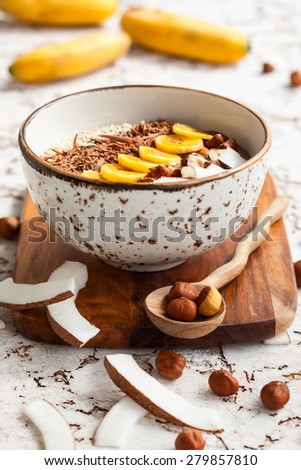 Chocolate hazelnut smoothie bowl topped with sliced banana, shredded coconut, chopped  chocolate, nuts and sesame seeds. Soft focus