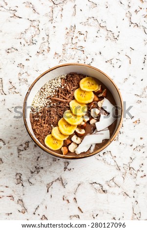 Chocolate hazelnut smoothie bowl topped with sliced banana, shredded coconut, chopped  chocolate, nuts and sesame seeds.