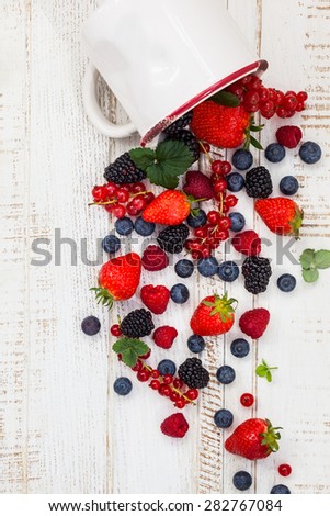 Fresh summer berries in vintage mug over wooden background,top view