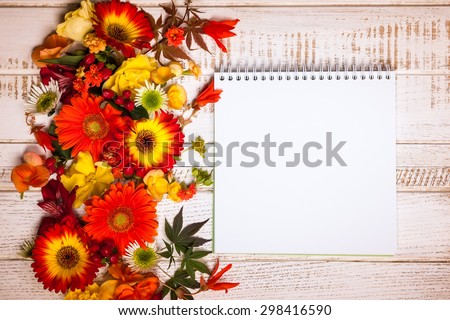 Blank notepad and autumnal flowers  on vintage wooden background. Top view with copy space