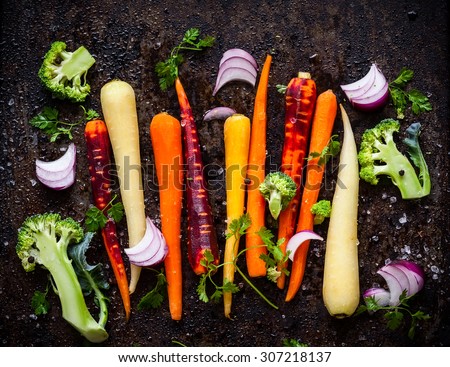raw rainbow carrot , broccoli and onion for roasting, on a baking tray