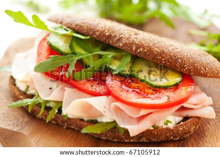 Sandwich with ham,tomato, cucumber and arugula on the wooden cutting board