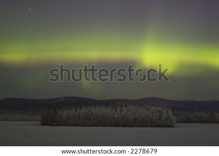 Some color of aurora borealis in the sky over distant frozen forest in Alaska