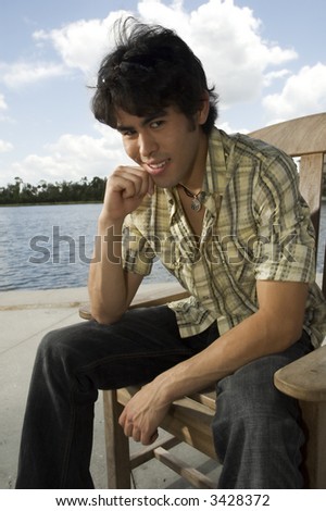 young man with mischievous grin on face sitting in front of a lake