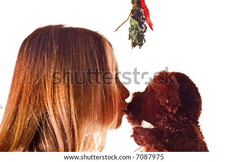 Young girl kisses her teddy bear under the mistletoe