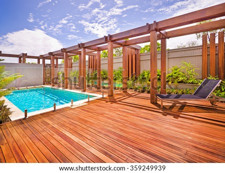 A beautiful view of pool in house in  a sunny day  with wooden floor with a bench
