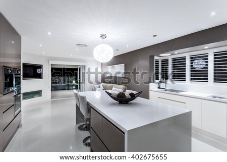 Luxury kitchen with wall oven cabinets next to the fancy items on the white counter top illuminated using round hanging lamp