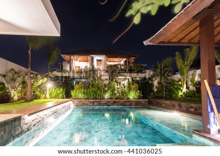 Modern house including a swimming pool in the middle illuminated with lights starting from the garden  at night