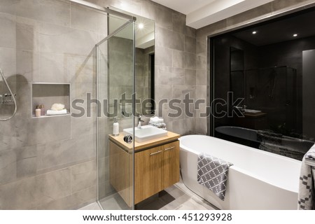 Modern bathroom with a shower and bathtub next to a mirror and tap with washstand illuminated at night