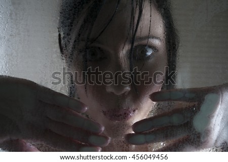 Portrait of a woman with dark hair looking through a steamy glass shower door