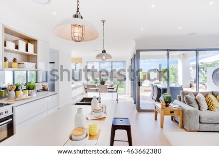 Modern kitchen with a dining and patio area including some utensils on counter top under the hanging lamps closely, the living room with sofa and pillows beside outdoor patio area with sunlight