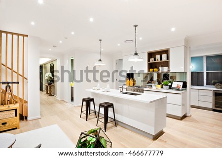 Modern kitchen with white walls illuminated by hanging lamps  at night beside the wooden hallway through the luxury house and stairs