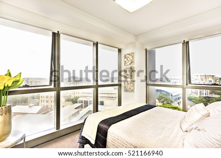 Colorful bed with pillows and city view, stylish room including abstract designs also town area can see through the window, luxurious look from windows and lightning, flower vase is more beautiful.
