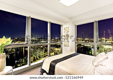 Comfortable bed near city view at night, stylish bedroom including abstract designs also town area can see through the window, luxurious look from attractive lamps near the glass panel.