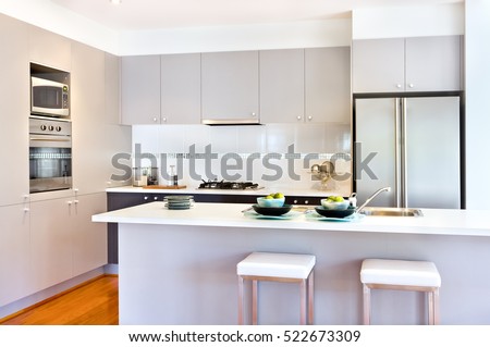 There are more wall cabinets or pantry cupboards with a stove and oven middle of it. The counter top is white next to the fridge, there are two small chairs in front of the counter.