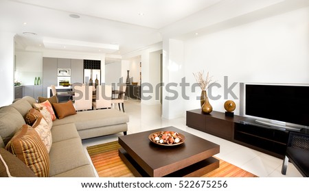 There are sofas and chairs with pillows in the modern living room including a creative wooden table with ornaments items on it. Long cupboard or TV stand with a vases close to the white wall,