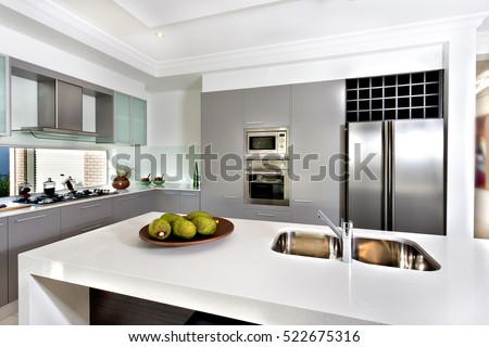 Counter top made in ceramic seen closely with fruits on a brown color clay dish next to the modern  silver faucet attached to the sink, the silver refrigerator .