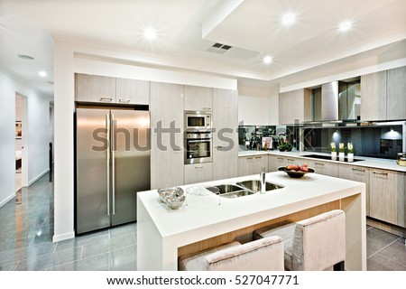 Modern kitchen counter top with a fridge and pantry giving a shiny look the house interior with flashing lights over the tile floor hallway