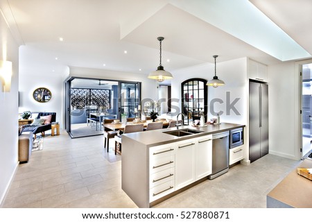 Modern kitchen with a dining room and patio area, there are flashing lamps hanging on the ceiling, over and tap with sink fixed to the counter cupboard. there are door and a hallway to outside patio