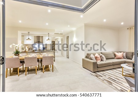 Modern House with a door entrance to the living room and dining kitchen including table set up beside the pillows on sofas at night with lights.