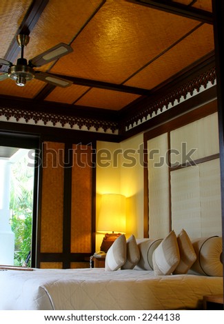 Hotel room in a tropical resort with a comfortable bed and wooden flooring. Concept: Travel and vacation.