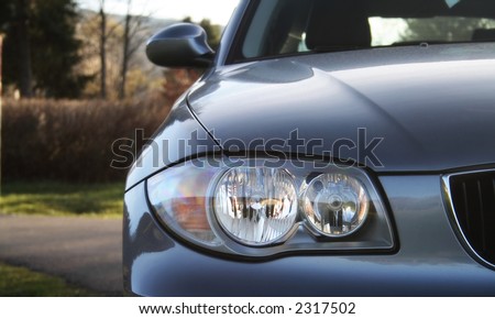 Front of a car with a blurred background. Metallic paint texture on car, not noise. Focus on lights.