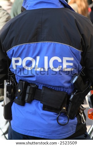 Back of a police officer in a blue generic uniform equipped with handcuffs, gun and walkie-talkie. Concept: Law & Order.
