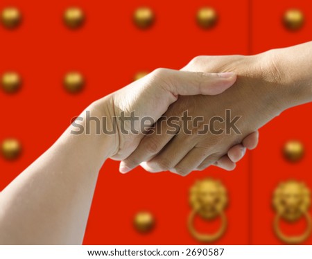 A pair of hands holding or shaking each other against a chinese red door. Concept: Business in china