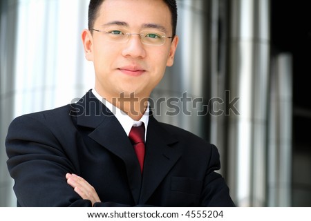 Good looking asian business man standing with arms folded.