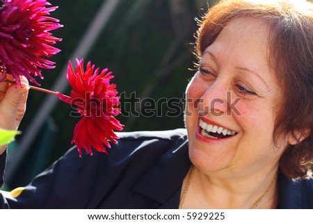 Elderly woman holding a red flower smiling and ready to smell it.